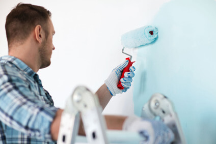 Peintre peignant un mur en bleu au rouleau
