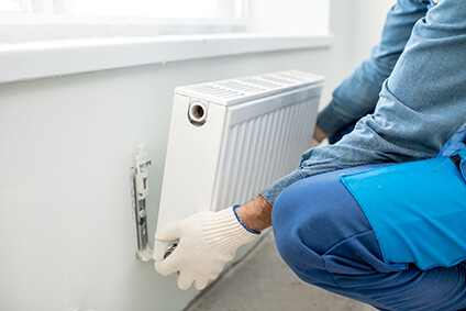 Chauffagiste plaçant un radiateur sur un mur sous une fenêtre